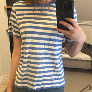 Blåvit randig t-shirt - Säljer en klassisk blåvit randig t-shirt med rund hals och korta ärmar. T-shirten har en relaxed passform och är gjord i mjuk bomull, perfekt för en chill och enkel stil. Passar till jeans eller shorts för en avslappnad look :) Knappt använd