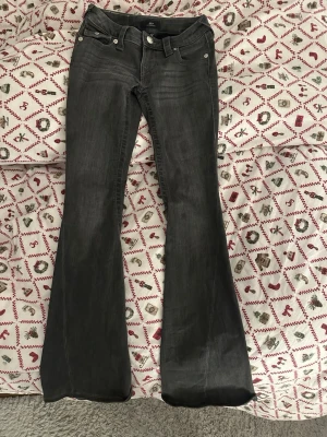 True Religion Joey Low Rise Flare Jeans - Säljer ett par mörkgrå True Religion Joey jeans med låg midja och flare-ben. Klassiska silverfärgade knappar och detaljerade bakfickor med lock och broderi. Jeansen är i stretchig denim och är super fina! Liten fläck på benet därav säljs dem för ett bättre pris❤️