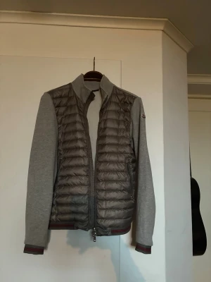 Grå Moncler pufferjacka med dragkedja - Snygg pufferjacka från Moncler i grått med quiltad kropp och mjuka, ljusgrå ärmar. Köpt på vongreven men är för liten! Skriv gärna om de finns funderingar!