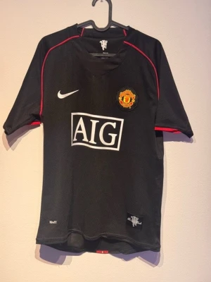 Manchester United Ronaldo tröja Nike S - Svart Manchester United t-shirt från Nike med röda detaljer, AIG-logga på bröstet och Ronaldo 7 på ryggen. Tillverkad i lätt polyester med korta ärmar och klubbmärke på bröstet. Perfekt för fotbollsfans som vill sticka ut på läktaren eller planen. PRISET ÄR EJ HUGGET I STEN!