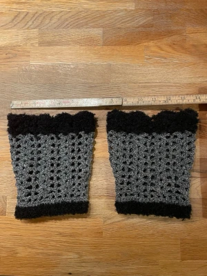 Fusk sockor /benvärmare i grått och svart - Säljer ett par handgjorda benvärmare i grått och svart. De är virkade med ett luftigt mönster och har fluffiga svarta kanter upptill och nedtill. Perfekta att dra över jeans eller leggings för extra värme och stil. Längd 19, bredd upptill 16, nertill 13 är lite elastiska. Helt nya. Går att beställa i valfri färg. 