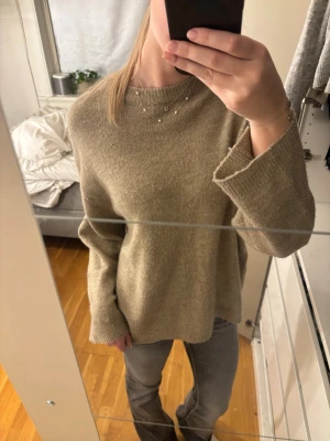 Beige stickad tröja 157 S - Mysig beige stickad tröja från 157 med rund halsringning och långa ärmar. Tröjan har en relaxed passform och ribbade muddar vid hals och ärmslut. Perfekt för lager på lager under kyliga dagar. Nopprig