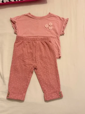 Jätte fin klickkläder 🌺 - Jätte fin  ett rosa set med t-shirt och byxor. T-shirten har volangärmar och blommor, byxorna är prickiga med knappar vid benslut.använd några gånger 