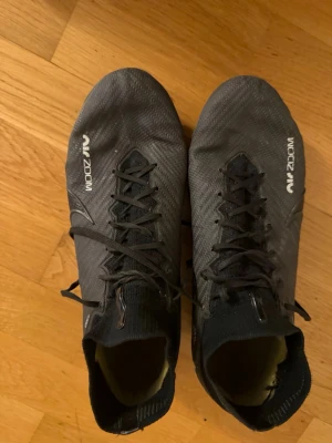 Nike Zoom svarta elite fotbollsskor  - Säljer ett par svarta Nike Zoom elite fotbollsskor med snörning och stickad strumpliknande kant. Skorna har en gulgrön innersula och slitstarka dobbar för gräsplan. Materialet är syntet med detaljer i stickad textil och coola loggor på sidan och sulan. Med väskan fast den är i bilen