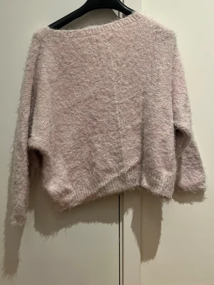 Ljusrosa fluffig stickad tröja - Supermjuk och fluffig ljusrosa stickad tröja med bred halsringning som kan bäras offshoulder. Tröjan har lång ärm och en loose passform, perfekt för mysiga dagar. Materialet känns riktigt gosigt och ger en chill vibe färgen är mer vibrant i verkligheten. 