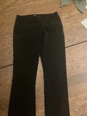 Lågmidjade kostymbyxor - Snygga svarta kostymbyxor, bootcut och klassiska fickor fram. Byxorna har bälteshällor och stängs med knapp och dragkedja. Sparsamt använda💕