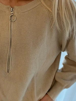 Beige stickad tröja Carin Wester M - Säljer en beige stickad tröja från Carin Wester i storlek M. Tröjan har en ribbad struktur, lång ärm och en snygg silverfärgad dragkedja med ringdetalj framtill. 