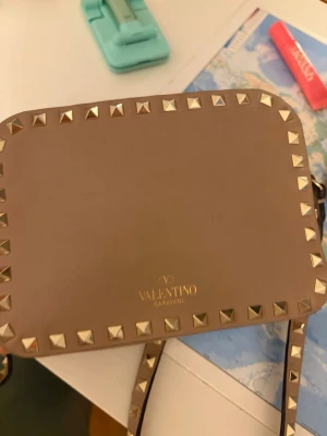 Valentino camera bag intressekoll - Vill kolla intressekoll på min valentino camera bag som är i bra skick men väldigt använd. De är smutsig inuti från tidigare ägare men går säkert att ta bort. Den har sina defekter. På bandet så har den gått upp på visa ställen ett exempel är bild 2 men dom andra delarna är nu limade och inte gått upp men kan såklart hända men ingeting jag tänker på när jag har på mig den. Utan på har den små markeringar om man kollar noggrant. Köpt här på Plick. 