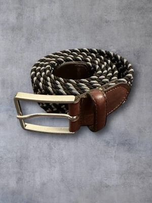 Saddler Flättat Bälte/Skärp - Snyggt flätat bälte från Saddler. Längd 105 cm/Bredd 3,5 cm. Material: Läder/Textil. Bältet är elastiskt