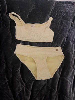Ljusgul ribbad bikini från KappAhl - Säljer en ljusgul ribbad bikini från KappAhl i storlek 146/152. OBS trosan är insydd lite i midjan så skulle att det mer är i storlek 134/140. Funderingar? Skriv till mig💕