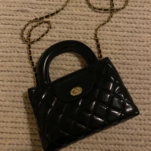 Svart väska - Svart glansig väska med gulddetaljer. Nyskick!