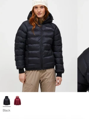 Svart dunjacka från Peak Performance - Säljer en svart dunjacka från Peak Performance med huva och dragkedja framtill. Jackan är quiltad med breda kanaler och har diskret logga på bröstet. Perfekt för kalla dagar och har en stilren look som funkar till det mesta. Den har lite slitage på ryggen men knappt något som syns.