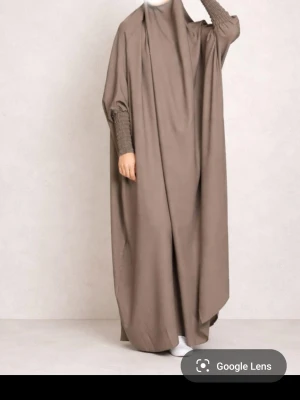 Jilbab med vida ärmar  - Säljer Jilbab med vida ärmar och smockade muddar. Klänningen har en lös passform och täcker hela kroppen, perfekt för dig som gillar modest stil. Materialet känns mjukt och faller snyggt. Finns i två färger mörkgrön och grå.