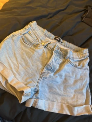 Ljusblå shorts från lager 157 - Säljer ett par ljusblå baggy shorts från lager 157 med hög midja och knappgylf. Klassisk femficksmodell med uppvikta benslut och snygga bakfickor. Perfekta till sommaren och lätta att matcha med allt.