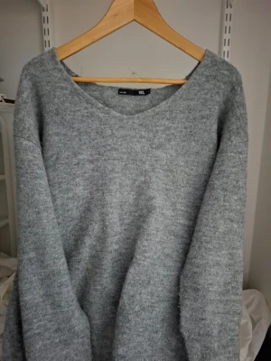 Grå stickad tröja från 157 - Mysig grå stickad tröja från 157 med avslappnad passform och rundad halsringning. Perfekt för lager på lager under kyliga dagar och enkel att matcha med jeans eller kjol.