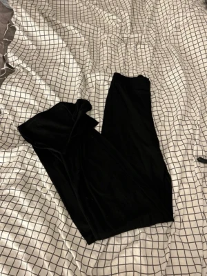 Svarta vida byxor från NA-KD - Säljer ett par svarta vida byxor från NA-KD i ribbat material och slits nere vid fötterna. Byxorna har hög midja och är riktigt mjuka och sköna, perfekta för en chill och snygg look. Passar dig som gillar loose fit och vill ha något enkelt men ändå stilrent.