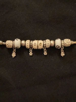 Pandora armband med berlocker - Säljer ett snyggt Pandora armband i silverfärg med flera berlocker i vitt och silver. Armbandet har detaljer som små blommor och fyrklöver som hänger, samt pärlor med mönster och stenar. Låset är hjärtformat och graverat. Perfekt accessoar för att lyfta din stil. Är dock ej säker om det är Pandora men jag tror det 💘 PRIS GÅR ATT DISKUTERA