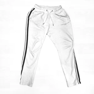 Vita mjukisbyxor Tommy Hilfiger S - Vita mjukisbyxor från Tommy Hilfiger i storlek S. Byxorna har svarta ränder längs sidorna, snörning i midjan och diskret logga på ena låret. Tillverkade i mjukt bomullsmaterial för maximal komfort och avslappnad stil.