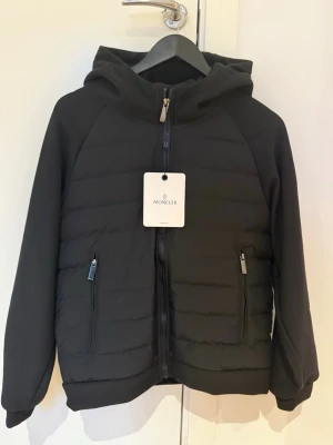 Svart Moncler pufferjacka med huva - Säljer en svart pufferjacka från Moncler med huva och två dragkedjeförsedda fickor. Jackan har Moncler-logga på ärmen och quiltad framsida. Stängs med dragkedja och har en clean, modern look som passar perfekt nu när vintern är här. Jackan är i storlek M men kan nog även passa i S. Priset går såklart att diskuteras. Kvitto finns!