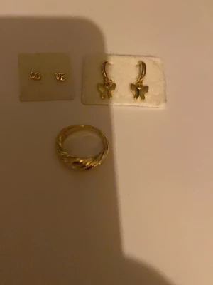 Guldguld smycken, aldrig använda! En ring och 2 par örhängen - Guldiga smycken, inte riktigt guld men färgen guld, en guldig ring vet inte vart ifrån men den är använd 1 gång, love örhängen som troligtvis är antagligen från glitter eller uropenn och ett par fjärils örhängen som också troligtvis är från glitter eller uropenn! Örhängerna är aldrig använda för jag fick dessa när jag fyller år men jag använder silvrigt så det är därför jag säljer dem!