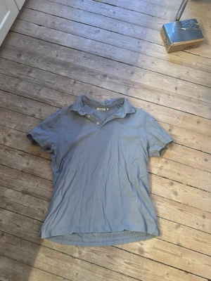 Blå pikétröja från Dobber - Säljer en klassisk blå pikétröja från Dobber med korta ärmar och två knappar vid kragen. Tröjan är gjord i mjuk bomull och har en avslappnad passform. Perfekt till jeans eller shorts för en enkel och snygg look. Storlek L