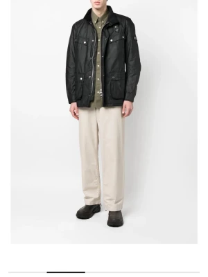 Svart Barbour International jacka M - Säljer en svart Barbour International jacka i klassisk modell med fyra stora fickor framtill, quiltat innerfoder och detaljer i metall. Jackan har dragkedja och knappar samt Barbour-logga på ärmen. Perfekt för dig som vill ha en tidlös och snygg jacka.