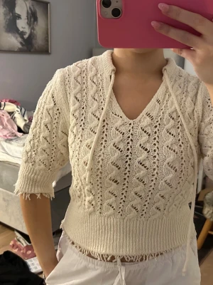 Vit stickad topp med snörning - Säljer en vit stickad topp med snyggt hålmönster och snörning i halsen. Tröjan har trekvartsärm och ribbad kant nedtill samt vid ärmslut. Perfekt för vår och sommar när du vill ha något luftigt men ändå mysigt.