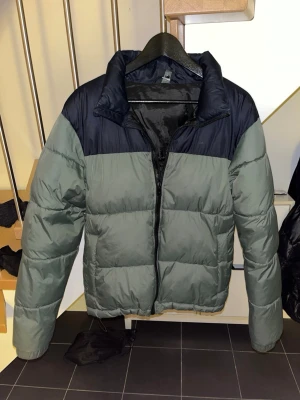 Pufferjacket Everest - Säljer en pufferjacka från Everest i grönt och svart. Jackan har hög krage, dragkedja framtill och är vadderad för extra värme. Perfekt för kyliga dagar och har en stilren, enkel design. Lite svårt att se färgen i desa bilder så skriv för fler bilder! Pris ej hugget i sten🪨