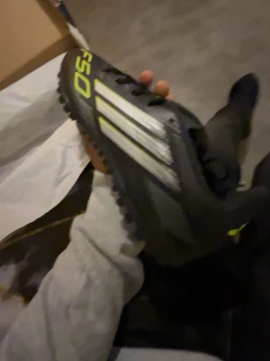 Adidas svarta f50  fotbollsskor  med gröna  detaljer - Säljer ett par svarta Adidas fotbollsskor med de klassiska tre vita ränderna på sidan och gula detaljer. Skorna har snörning och en sula med dobbar som passar perfekt för spel på konstgräs. Snygg och sportig design som sticker ut på planen.