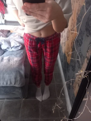 Rutiga röda mjukisbyxor från KappAhl - Säljer ett par röda mjukisbyxor från KappAhl med klassiskt rutigt mönster i vitt och mörkblått. Byxorna har en enkel, rak passform och är tillverkad i mjukt bomullstyg. Perfekt för dig som gillar en chill och tidlös stil.