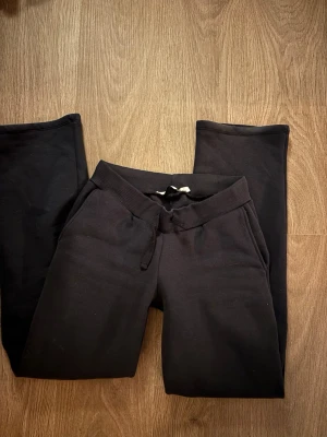 Lågmidjade mjukisbyxor med snörning - Ett par svarta mjukisbyxor med resår i midjan och snörning framtill. Byxorna har raka ben och sidofickor, perfekta för chill dagar eller när du vill vara bekväm. Tillverkade i mjukt bomullsmaterial.