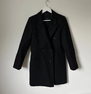 Svart Massimo Dutti kappa - Elegant svart kappa med dubbelknäppning. Klassisk modell som passar både till vardags och fest. 5G5