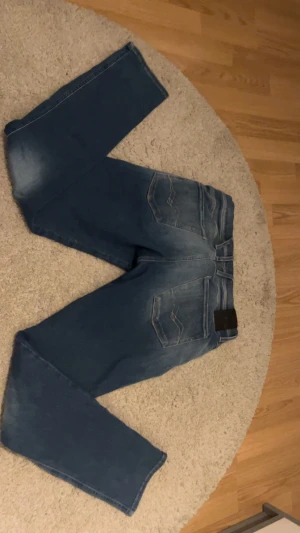 Blå Replay Anbass jeans straight fit - Snygga blå Replay Anbass jeans med straight fit och klassisk femficksdesign. Jeansen har en cool tvätt med ljusare partier framtill och bak, samt detaljerade sömmar på bakfickorna. Perfekt för dig som gillar en avslappnad men stilren look.