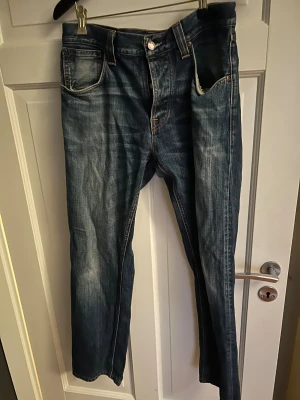 Blå jeans från Nudie Jeans Co W32 L34 - Snygga blå jeans från Nudie Jeans Co med klassisk femficksdesign och coola orangea sömmar på bakfickorna. Jeansen har en rak passform och är tillverkade i slitstarkt denim med lätt tvättad look. Perfekt för dig som gillar street och casual stil.