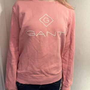 Rosa GANT sweatshirt XS - Säljer en rosa sweatshirt från GANT i storlek XS. Tröjan har broderad logga framtill, rund halsringning och ribbade muddar vid ärmslut och nederkant. Perfekt för dig som gillar klassisk och stilren streetwear. Obs en lite märkning i nacken.