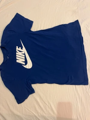 Blå Nike t-shirt med stor logga - Snygg blå t-shirt från Nike i storlek S med stor vit Nike-logga och swoosh på bröstet. Klassisk rund hals och korta ärmar. 