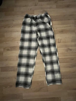 Rutig byxa från H&M i svartvitt - Snygga rutiga byxor från H&M i svart och vitt. Byxorna har elastisk midja och är tillverkade i mjuk bomull, perfekta för en chill och avslappnad stil. Passar dig som gillar loose fit och vill ha något bekvämt men ändå trendigt.