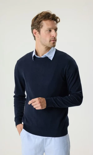 Mörkblå stickad tröja med rund hals - En helt oanvänd mörkblå stickad tröja med rund halsringning och ribbade muddar. Tröjan har en klassisk passform och är perfekt att bära över en skjorta. Materialet är mjukt och ger en clean look.