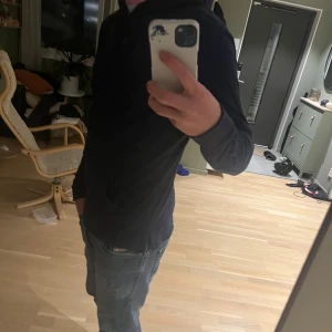 Marinblå hoodie från Polo Ralph Lauren - Säljer en marinblå hoodie från Polo Ralph Lauren med klassisk röd logobrodyr på bröstet. Tröjan har huva med snörning och är tillverkad i mjuk bomull. Långärmad och med normal passform, perfekt för chill dagar.