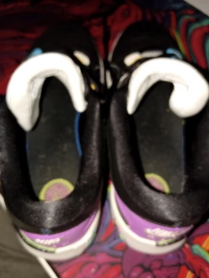 Nike Air sneakers med lila detaljer - Unika Nike Air sneakers med lila, svart och vita paneler samt färgglada detaljer på sulan. Skon har signatur på plösen och coolt mönstrad innersula. Snygg kontrast mellan färgerna och klassisk Nike Air-logga bak. Perfekt för dig som vill sticka ut med dina sneakers. OBS liten skada på båda skornas sulla