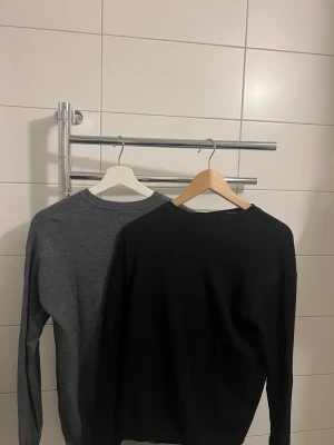 2-pack basic tröjor Lindex 158/164 - Två stilrena basictröjor från Lindex i storlek 158/164. En är helsvart och en är mörkgrå, båda med rund hals och långa ärmar. Perfekta att matcha med jeans eller kjol. Materialet är mjukt och skönt, passar för både höst och vinter.