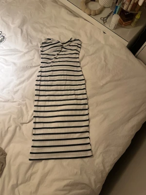Randig axelbandslös klänning - Säljer en snygg axelbandslös klänning med svartvita horisontella ränder. Klänningen är figurnära och har en twistad detalj vid bysten. Perfekt för dig som gillar en stilren och trendig look. 