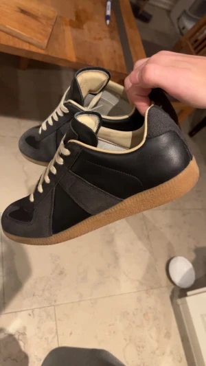 Svarta sneakers från Maison Margiela - Maison Margiela Gats skor, svart skinn och grå mocka. Är en äldre mer limiterad modell. Skorna köptes för ca 5 år sen. Skorna är i nyskick och har bara används ett fåtal gånger. Storlek 40 men passar även 41. Box och 2 dustbags ingår, kvitto finns tyvärr ej då dom köptes på vinted. Perfekta skor för dig som vill vara lite unik och inte ha skor som alla andra har! Tveka inte att skriva vid minsta fråga! ✉️🙌