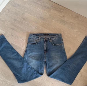 Nudie Jeans - Säljer ett par klassiska blå skinny jeans från Nudie Jeans med hög midja. Jeansen har fem fickor, orangea sömmar och Nudie-logga på bakfickan. Tillverkade i mjukt denimtyg med snygg tvättad look och raka ben.