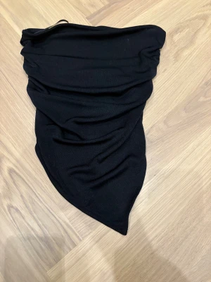 Svart halsduk från Gina Tricot - Svart halsduk från Gina Tricot i storlek XS. Snygg trekantig form med rynkade detaljer som ger en cool look. Materialet är mjukt och stickat, perfekt för att hålla värmen under kyliga dagar. Enkel att matcha med din jacka eller hoodie.