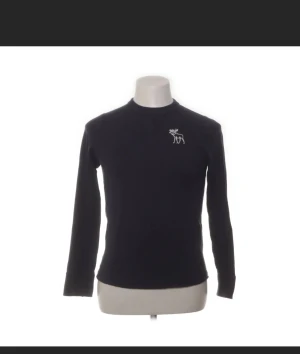 Mörkblå långärmad tröja Abercrombie - Snygg mörkblå långärmad tröja från Abercrombie med vit älglogga på bröstet. Tröjan har rund hals och är gjord i mjuk bomull, perfekt för chill dagar. Enkel och stilren design som funkar till jeans eller shorts.