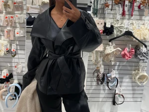 Svart omlott skinnjacka med bälte - Säljer en svart skinnjacka med bred krage och omlott-design från gina. Jackan har ett matchande bälte i midjan som knyts för att ge en snygg siluett. Materialet är slätt och ger en cool vibe, perfekt för dig som gillar statement-plagg.