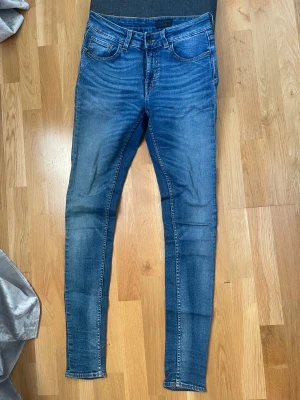 Blå skinny jeans från Tiger of Sweden - Snygga blå jeans från Tiger of Sweden med klassisk femficksdesign och bruna detaljer på bakfickan. Jeansen har skinny passform, mid waist. Lite stretchiga vid benen. 