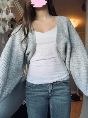 Grå stickad kofta från Gina Tricot - Säljer en ljusgrå stickad kofta från Gina Tricot i storlek M. Koftan har breda, ribbade ärmar och en loose passform som ger en chill vibe. Perfekt att slänga över en topp när det är lite kyligt. Enkel och snygg design utan knappar eller dragkedja.