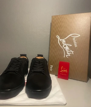 Svarta sneakers från Christian Louboutin - Snygga svarta sneakers från Christian Louboutin med klassisk röd sula och diskret logga. Skorna har rund tå, snörning och är tillverkade i skinn och mocka för en lyxig känsla. Perfekta för dig som vill sticka ut med exklusiva detaljer.